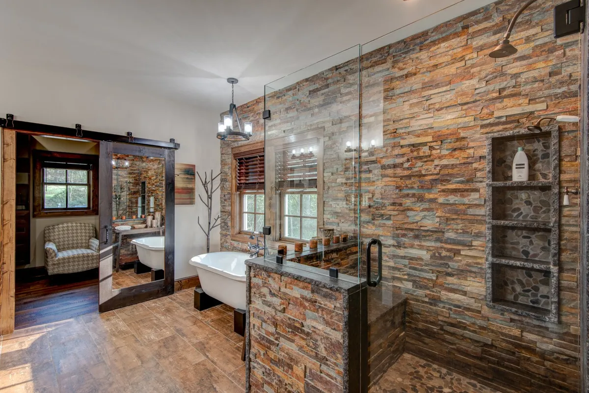A luxurious bathroom with a freestanding soaking tub, stone accent wall, and glass shower enclosure. The wooden sliding barn door and abundant natural light add to the spa-like ambiance, perfect for unwinding after a day of adventure.