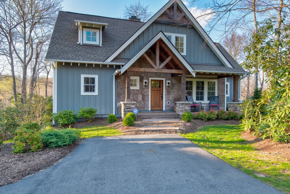 This image displays the inviting front door of Bluebird Cottage, flanked by a charming stone facade, ample porch seating, and a beautifully landscaped garden. The scene hints at a tranquil and welcoming entry point, surrounded by greenery and a peaceful outdoor ambiance.