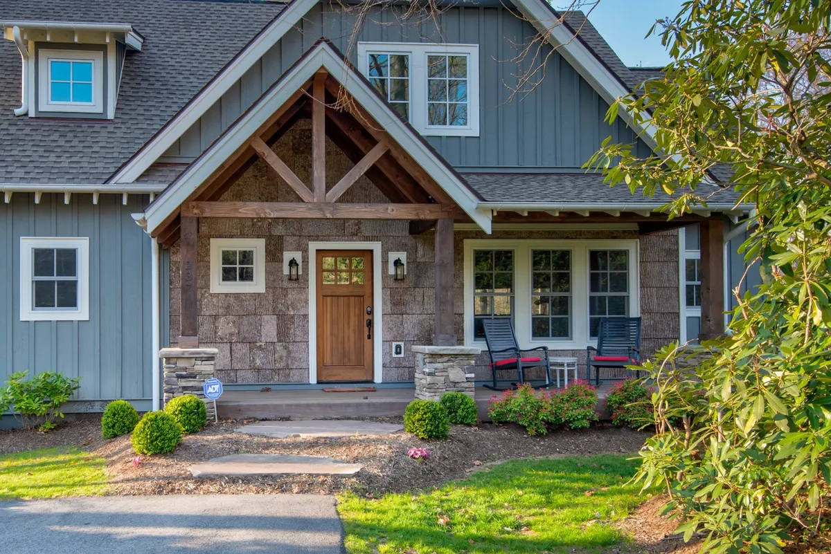 An inviting exterior view of Bluebird Cottage’s front entrance, featuring charming stone accents, a welcoming front door, and comfortable porch seating. The well-kept garden and architectural details set a friendly, homey tone, while the porch hints at relaxing outdoor moments.