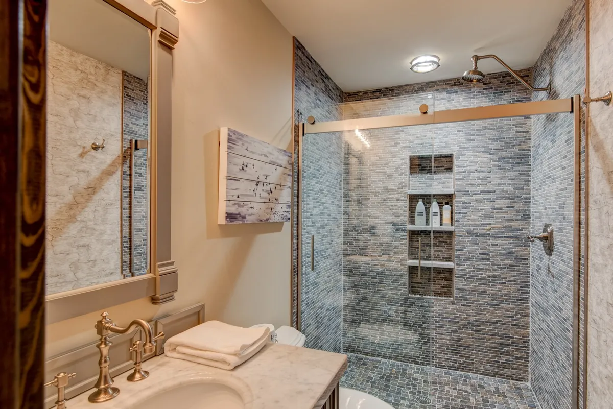 A serene ensuite bathroom showcasing a glass shower enclosure, marble countertop, and decorative wall art. The clean lines and natural hues create an elegant, tranquil environment that elevates daily routines into soothing rituals.