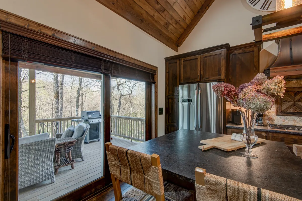 A bright kitchen scene with a large island, fresh flowers in a vase, stainless steel appliances, and a view extending to an outdoor seating area. Natural light pours in, suggesting easy transitions between indoor comfort and outdoor adventure.