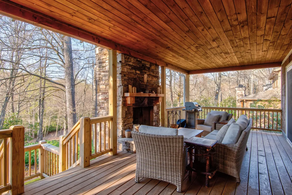 An inviting outdoor seating area featuring a stone fireplace, wooden ceiling, and grill—ideal for relaxing evenings, social gatherings, or warm fireside conversations. The backdrop includes sunset lighting, suggesting year-round comfort outdoors.