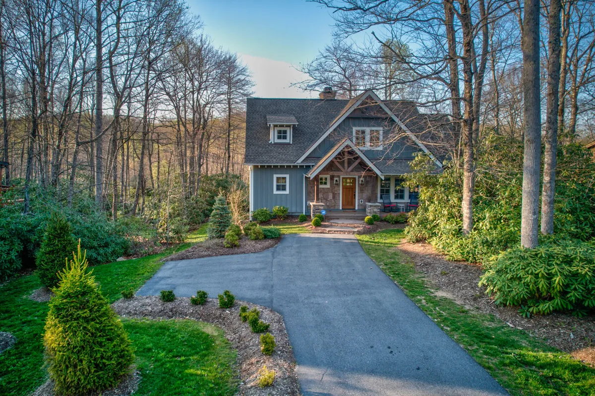 This image shows the cottage's exterior, including the house, an expansive front porch, and surrounding landscaped garden. The warm, inviting mood suggests opportunities for outdoor gatherings, sunset views, and peaceful moments amidst nature.